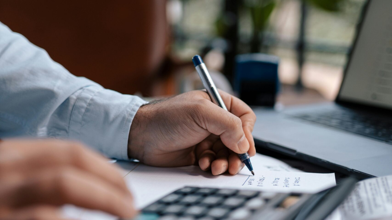 Free A person calculating finances with a calculator and pen on a desk indoors. Stock Photo