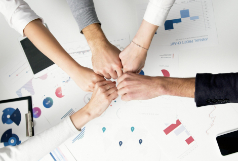 Free Colleagues celebrate success with a fist bump over financial charts depicting teamwork and unity. Stock Photo