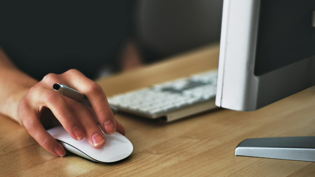 Free A hand using a wireless mouse at a modern desk setup with a computer and keyboard. Stock Photo