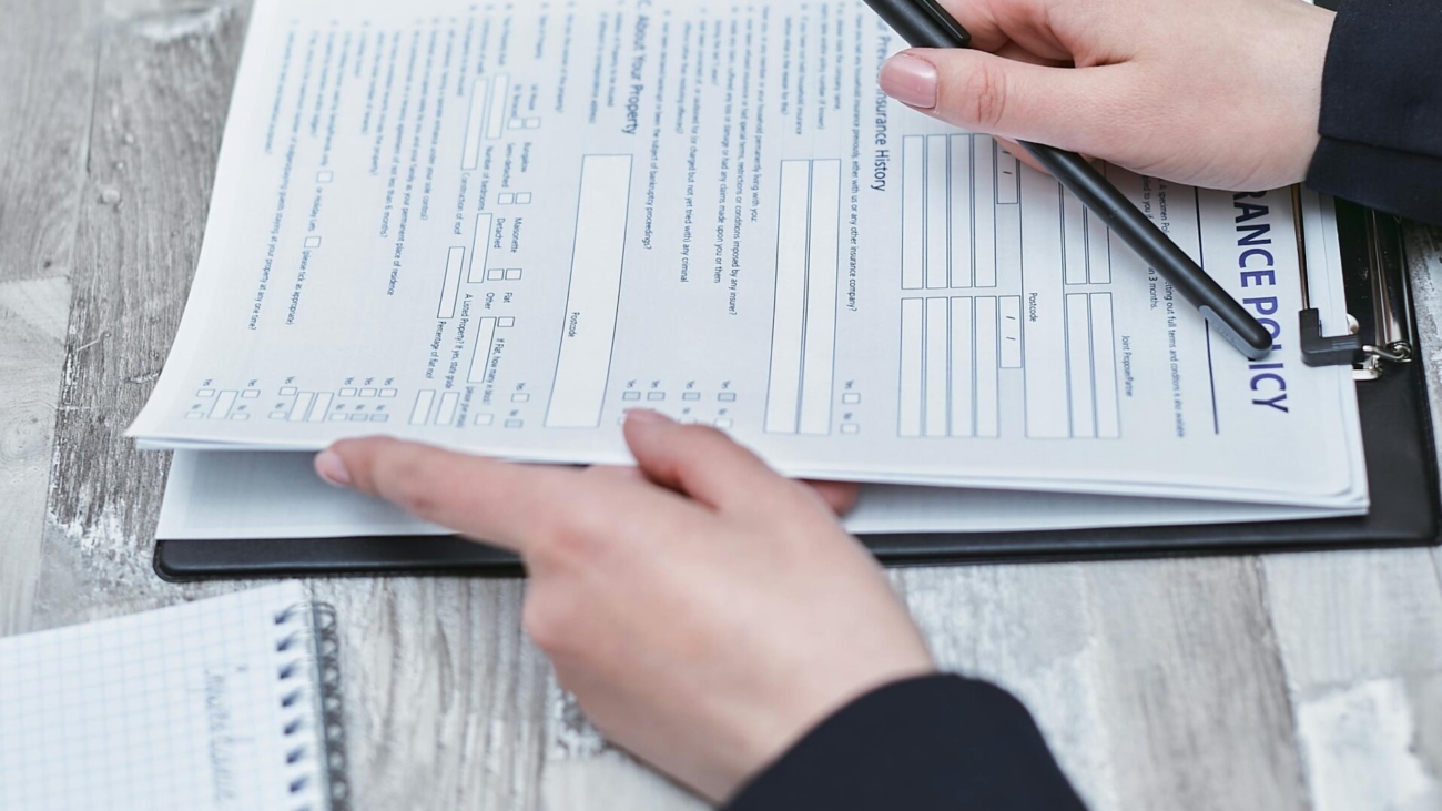 Free Close-up of hands analyzing insurance policy paperwork with pen on table. Stock Photo