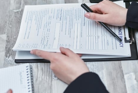 Free Close-up of hands analyzing insurance policy paperwork with pen on table. Stock Photo